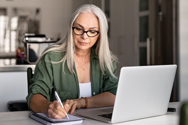 Mature woman at laptop making notes about insurance, like the products carried by the Medicare Store.