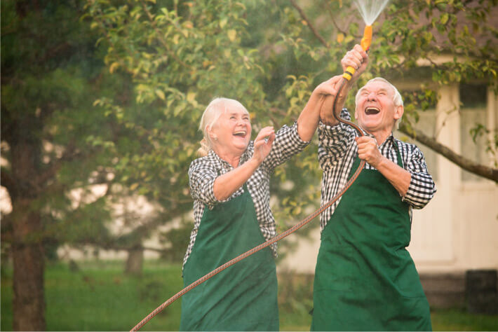 Happy mature couple, like those served with Medicare insurance by Agency4RED, playing in the garden hose.