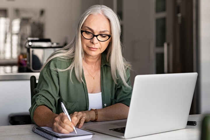 Mature woman at laptop making notes about insurance, like the products carried by the Medicare Store.