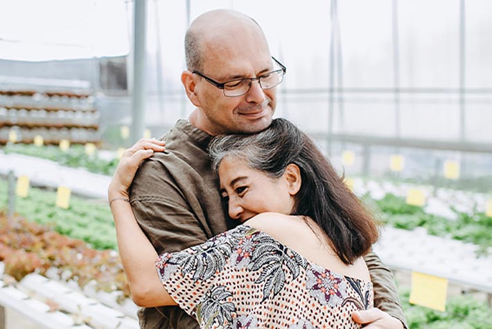 Mature couple embracing in greenhouse, satisfied with their new Medicare coverage in Texas.
