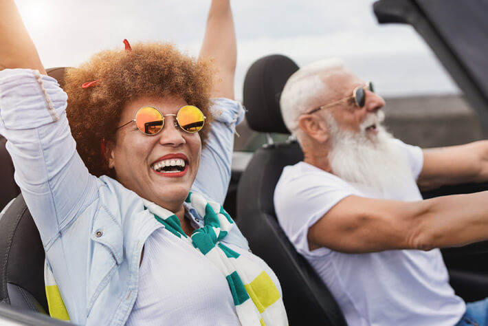 Happy mature couple, like those served with Medicare insurance by Agency4RED, enjoying a convertible ride.